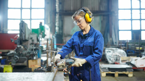 Potrait of modern female worker cutting metal at industrial plant or garage, copy space